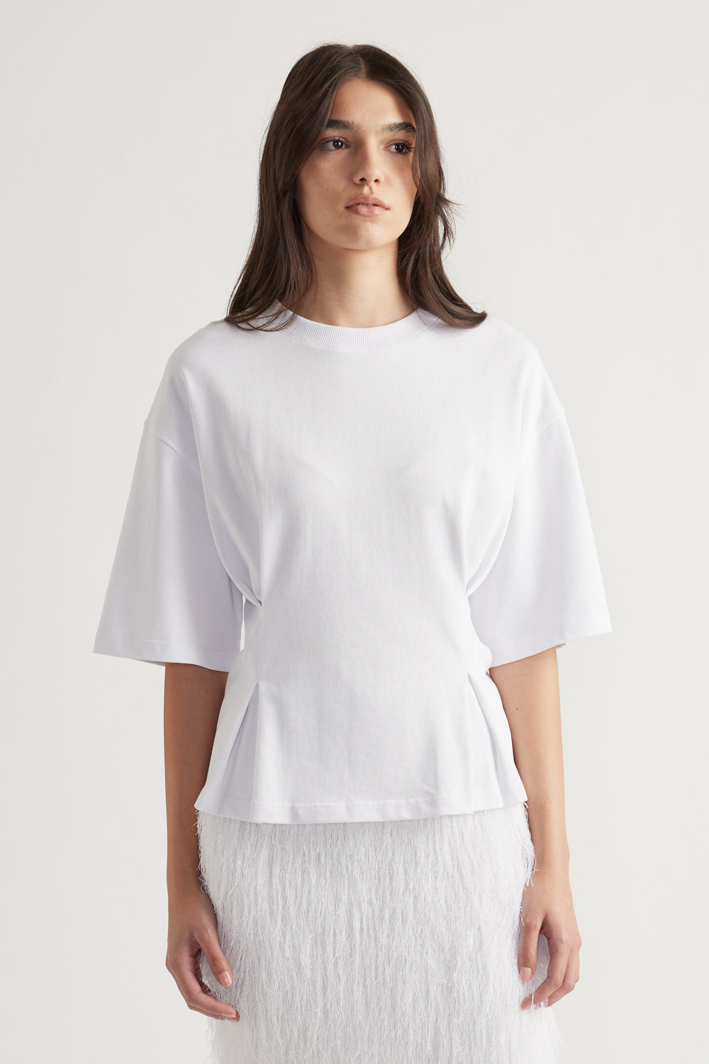 Woman wearing a bright white structured tee with wide sleeves paired with a textured white skirt for a clean look.