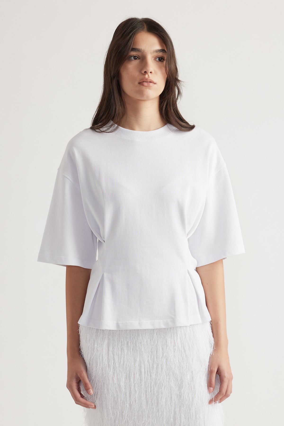 Woman wearing a bright white structured tee with wide sleeves paired with a textured white skirt for a clean look.