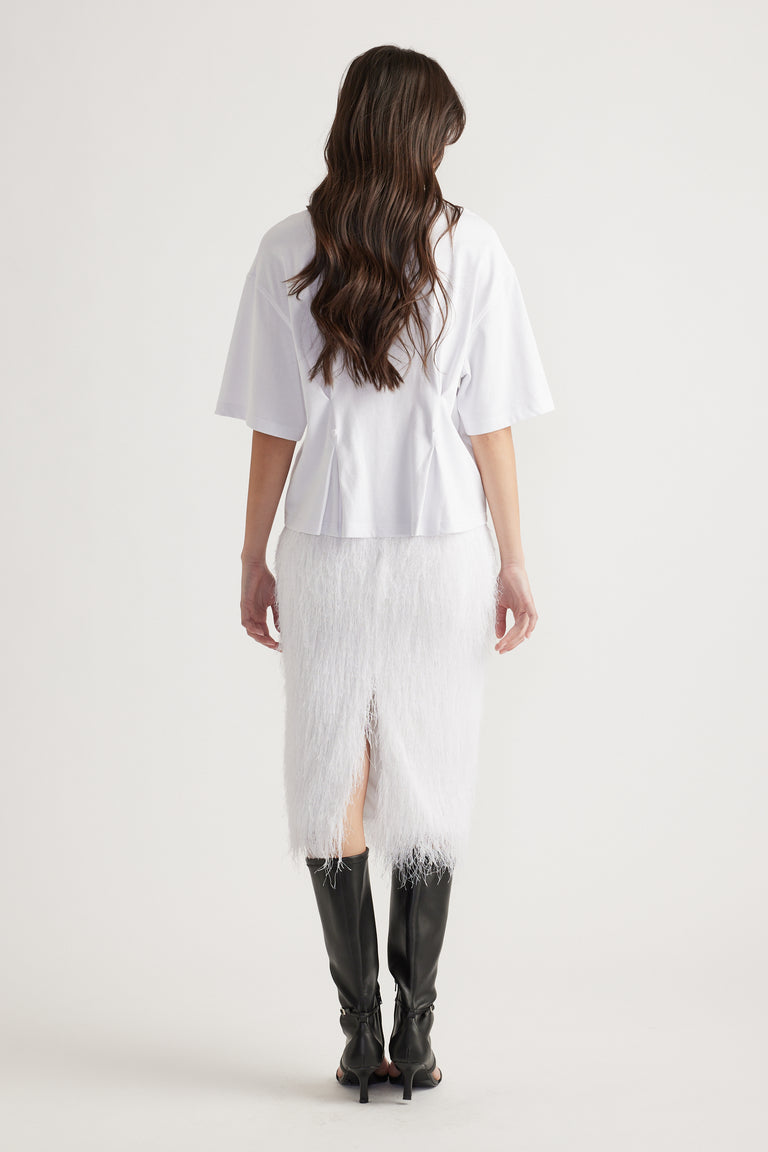 Woman with loose waves wearing a white structured tee paired with a textured white midi skirt and black knee-high boots.
