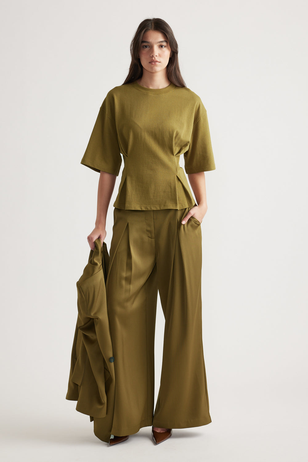 Woman wearing an olive structured tee with wide-leg pants holding a matching blazer for a polished look