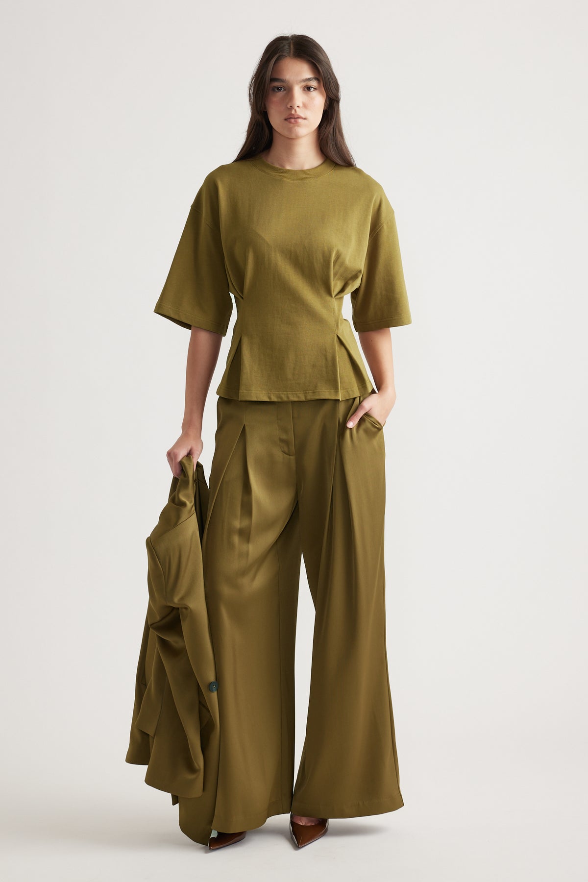 Woman wearing an olive structured tee with wide-leg pants holding a matching blazer for a polished look