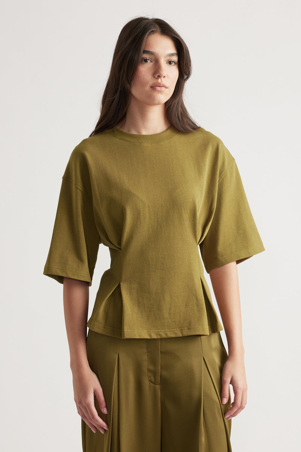 Woman wearing a structured olive green tee with wide sleeves paired with matching high-waisted pleated pants