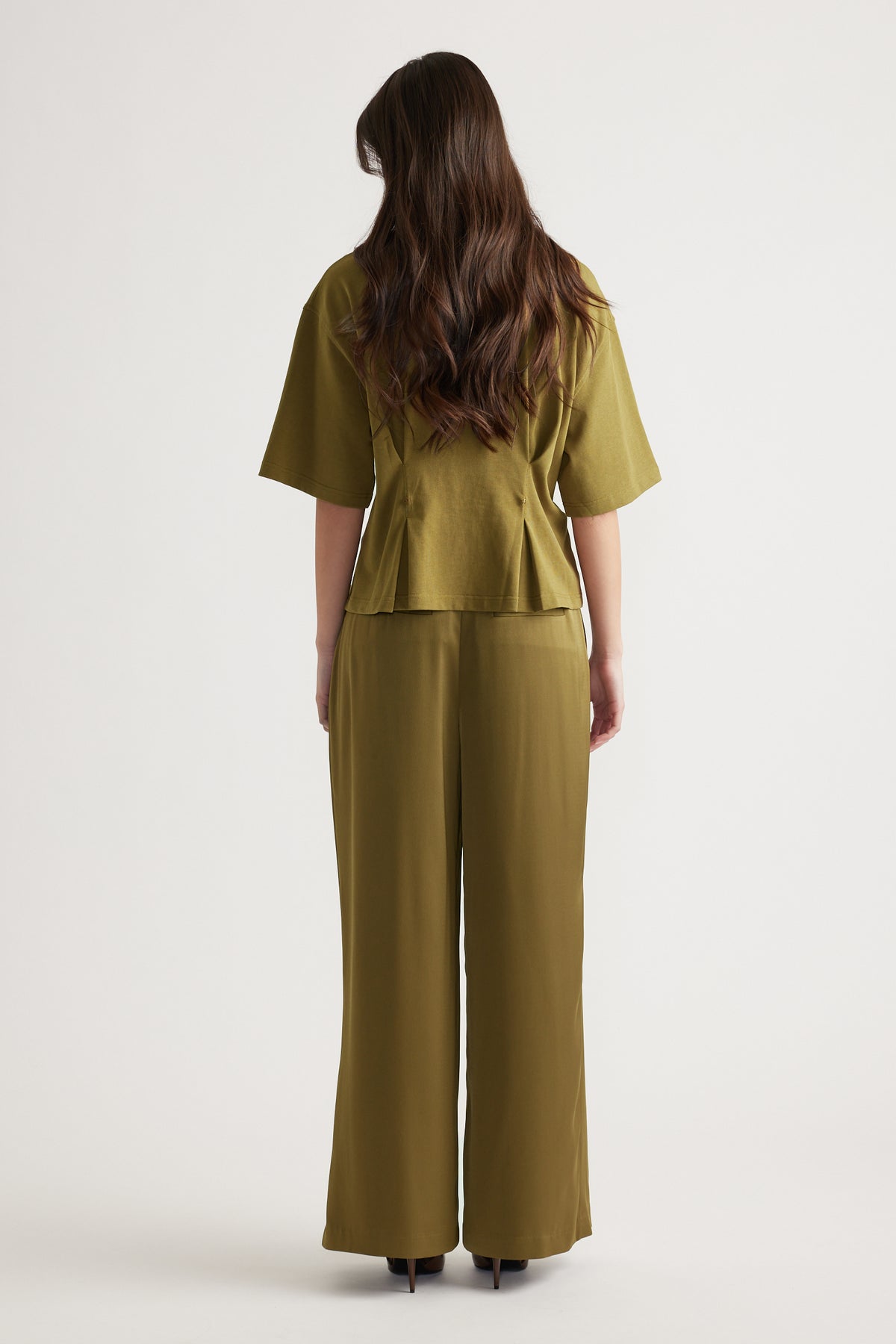 Woman shown from behind wearing an olive green structured top with wide sleeves and matching wide-leg pants