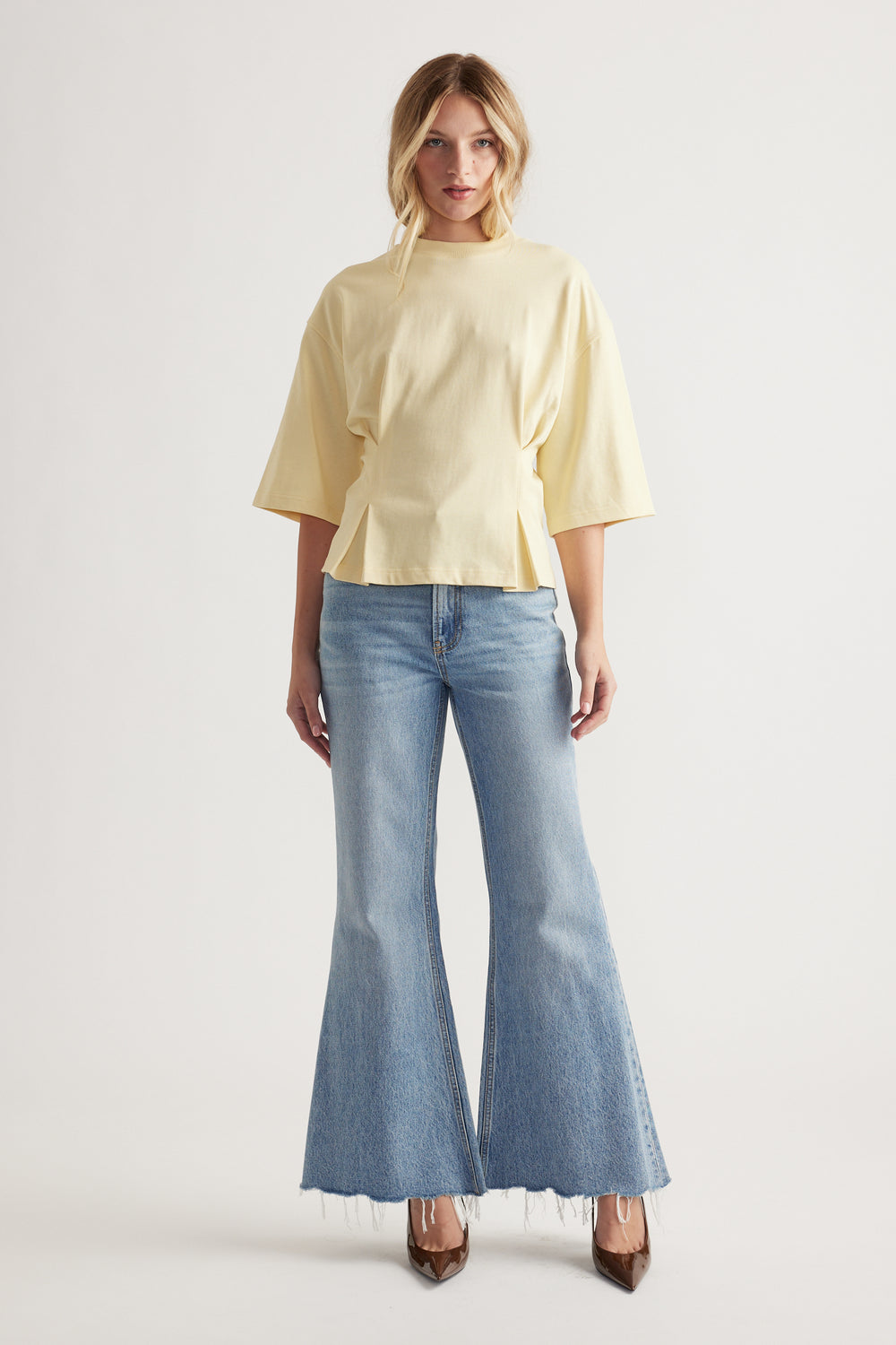 Woman wearing a pale yellow structured tee with wide half sleeves paired with light wash flared raw hem jeans and heels