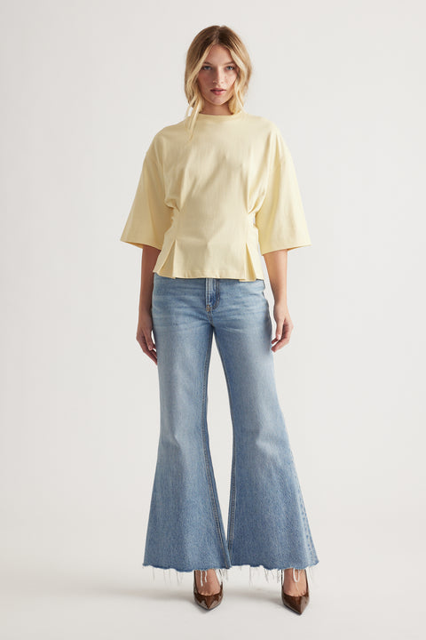 Woman wearing a pale yellow structured tee with wide half sleeves paired with light wash flared raw hem jeans and heels