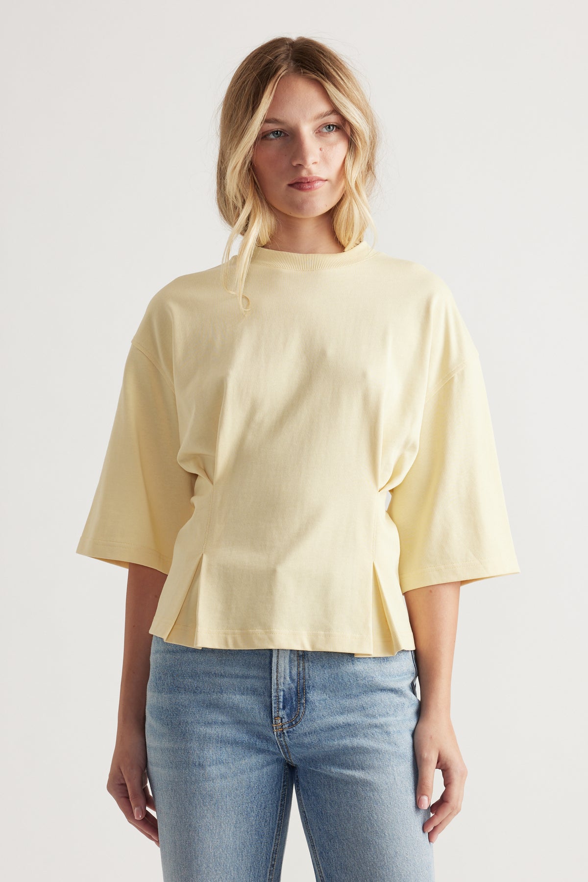 Woman wearing a soft yellow structured tee with wide sleeves paired with light blue high-rise denim jeans