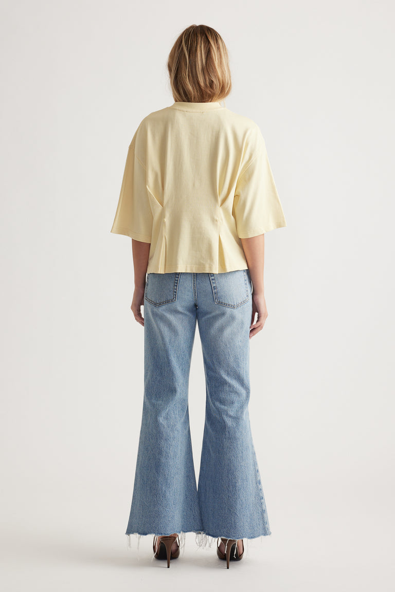 Woman wearing a pale yellow structured top paired with light wash flared denim jeans and black heels, back view.