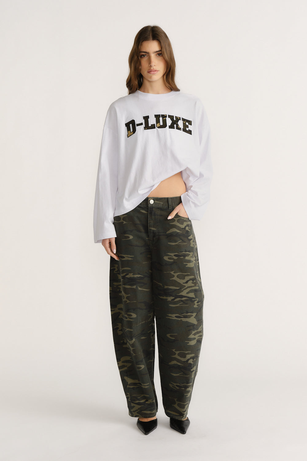 Woman wearing relaxed camo pants paired with a loose white long-sleeve tee featuring bold printed lettering.