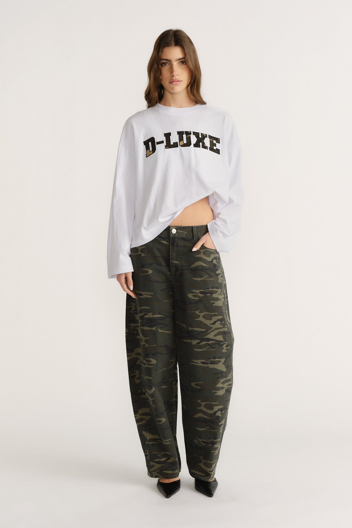 Woman wearing relaxed camo pants paired with a loose white long-sleeve tee featuring bold printed lettering.