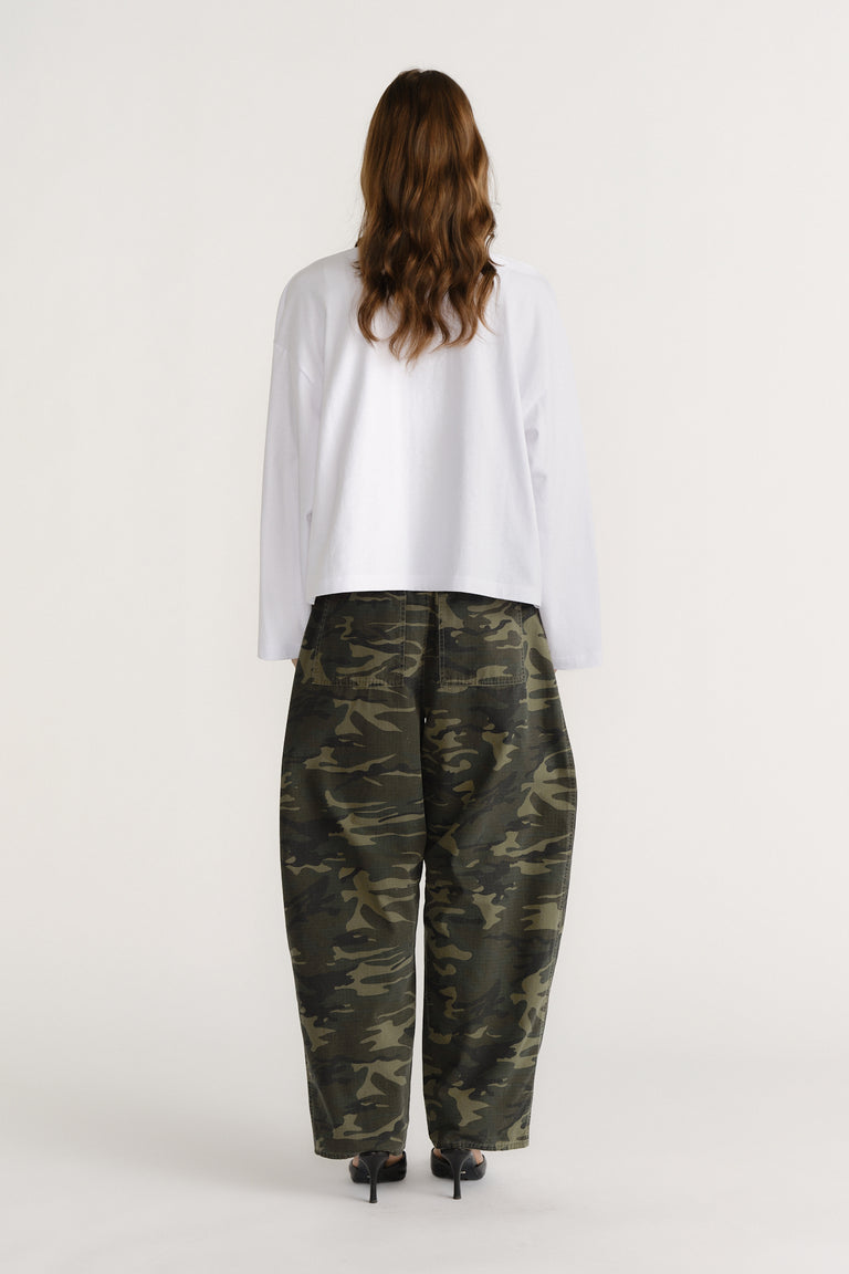 Woman wearing loose-fitting camo pants paired with a relaxed white long-sleeve top and black heels.