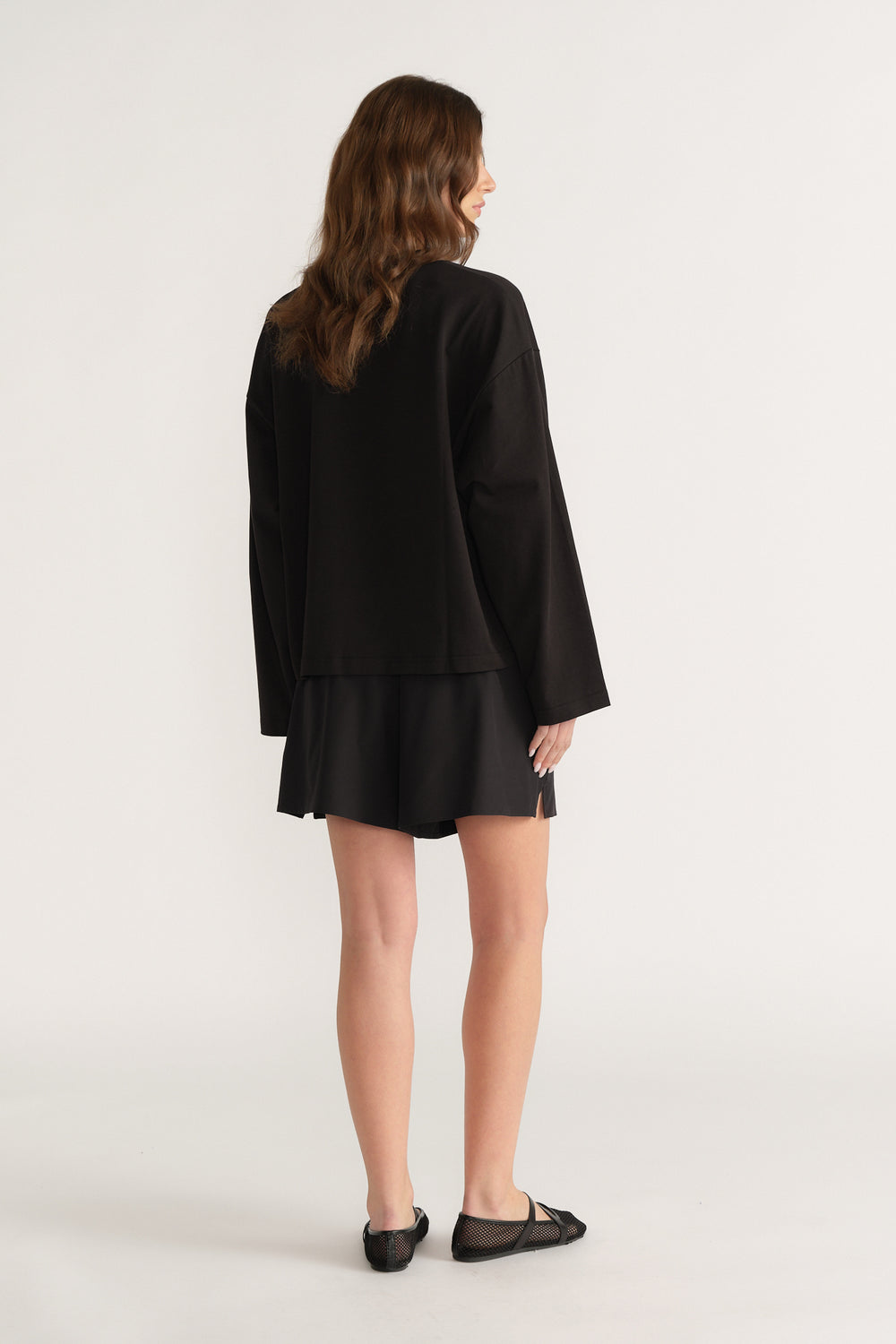 Back view of a woman wearing a black oversized long sleeve tee with black shorts and ballet flats