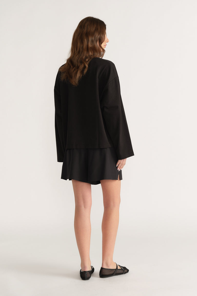 Back view of a woman wearing a black oversized long sleeve tee with black shorts and ballet flats
