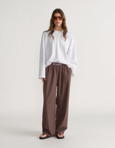 Woman wearing an oversized white D-Luxe long sleeve tee with brown wide-leg pants and sunglasses