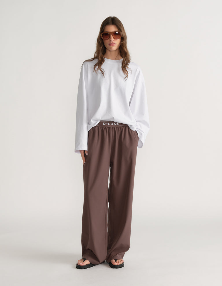 Woman wearing an oversized white D-Luxe long sleeve tee with brown wide-leg pants and sunglasses