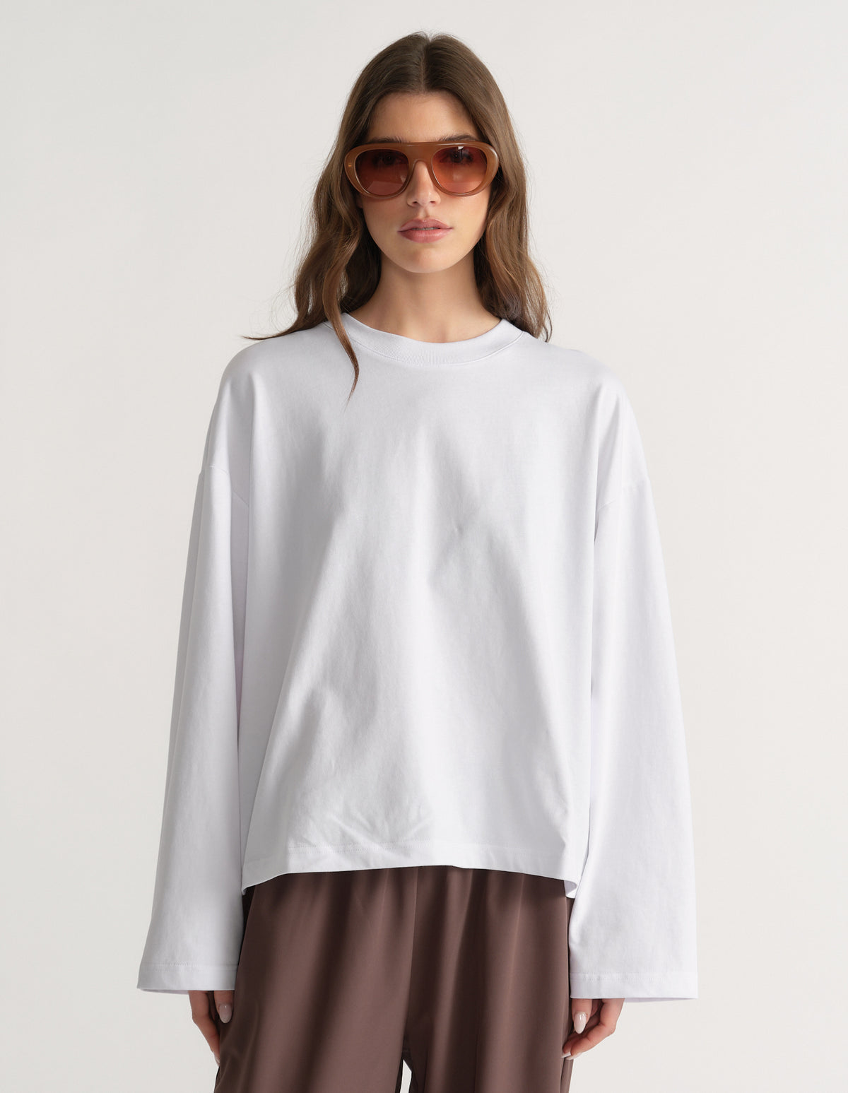 Woman wearing an oversized white long sleeve tee with brown pants and sunglasses