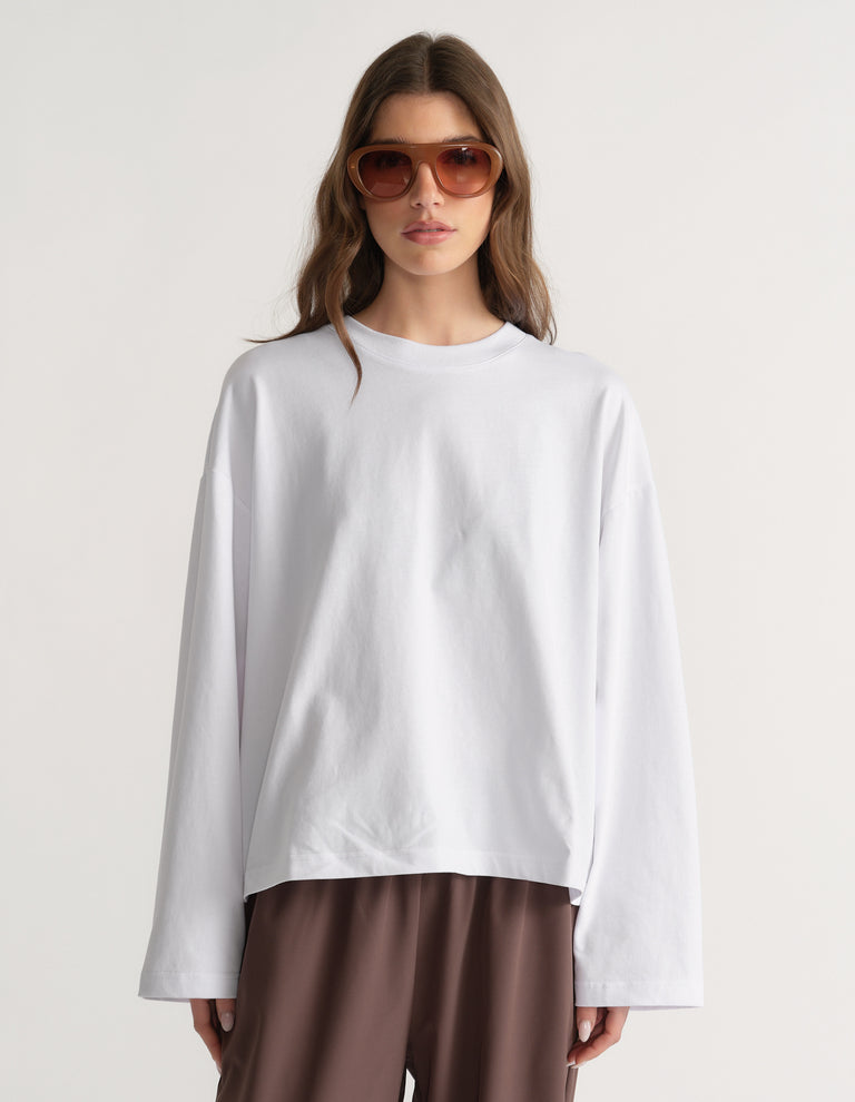 Woman wearing an oversized white long sleeve tee with brown pants and sunglasses