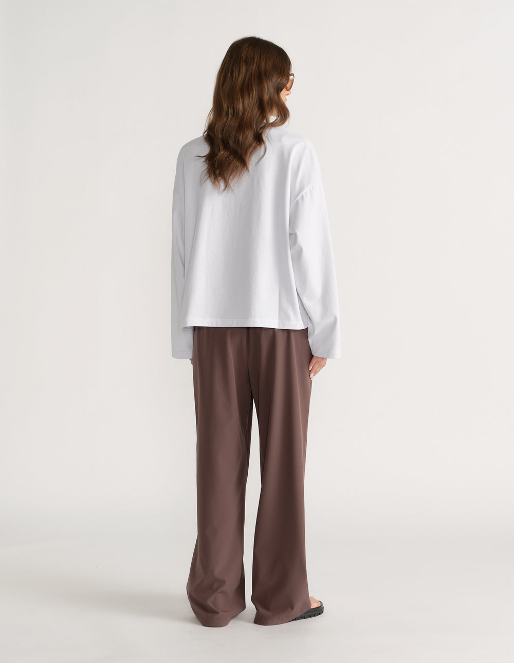 Back view of a woman wearing an oversized white long sleeve tee with brown wide leg pants