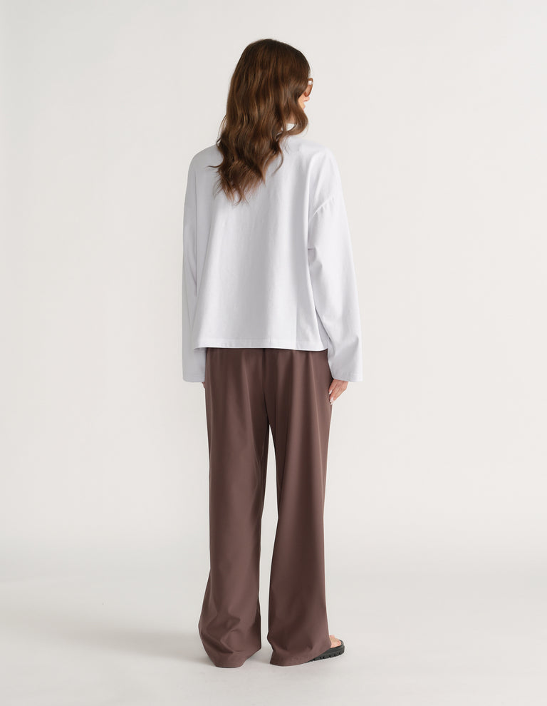 Back view of a woman wearing an oversized white long sleeve tee with brown wide leg pants