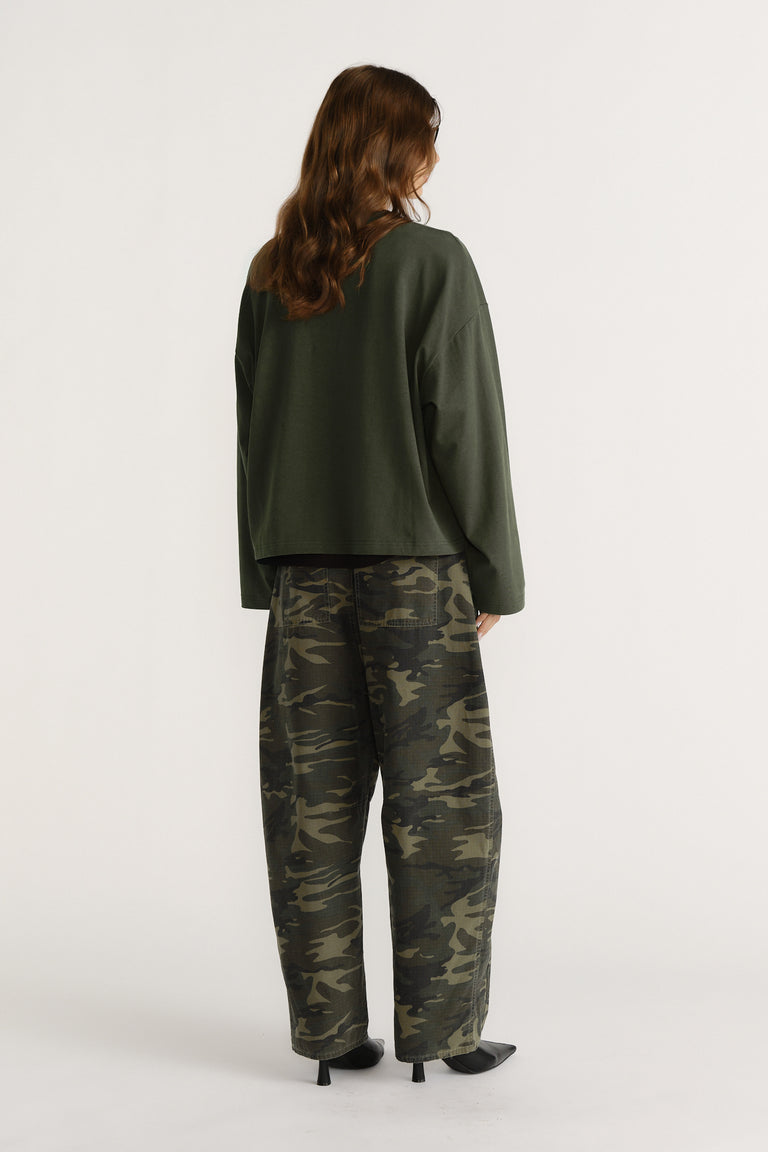 Woman seen from behind wearing boxy dark green long sleeve tee paired with loose camo print pants and black heels