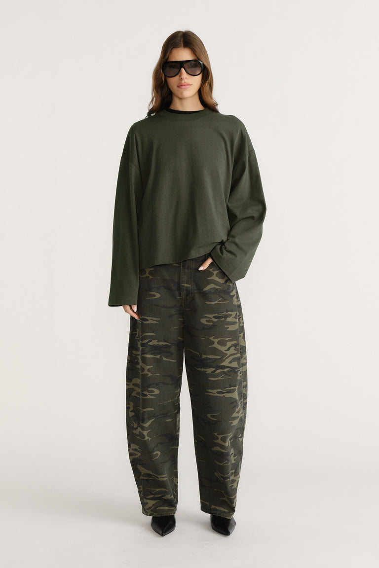 Woman wearing oversized dark green long sleeve tee with wide sleeves paired with loose camo pants and black pointed shoes