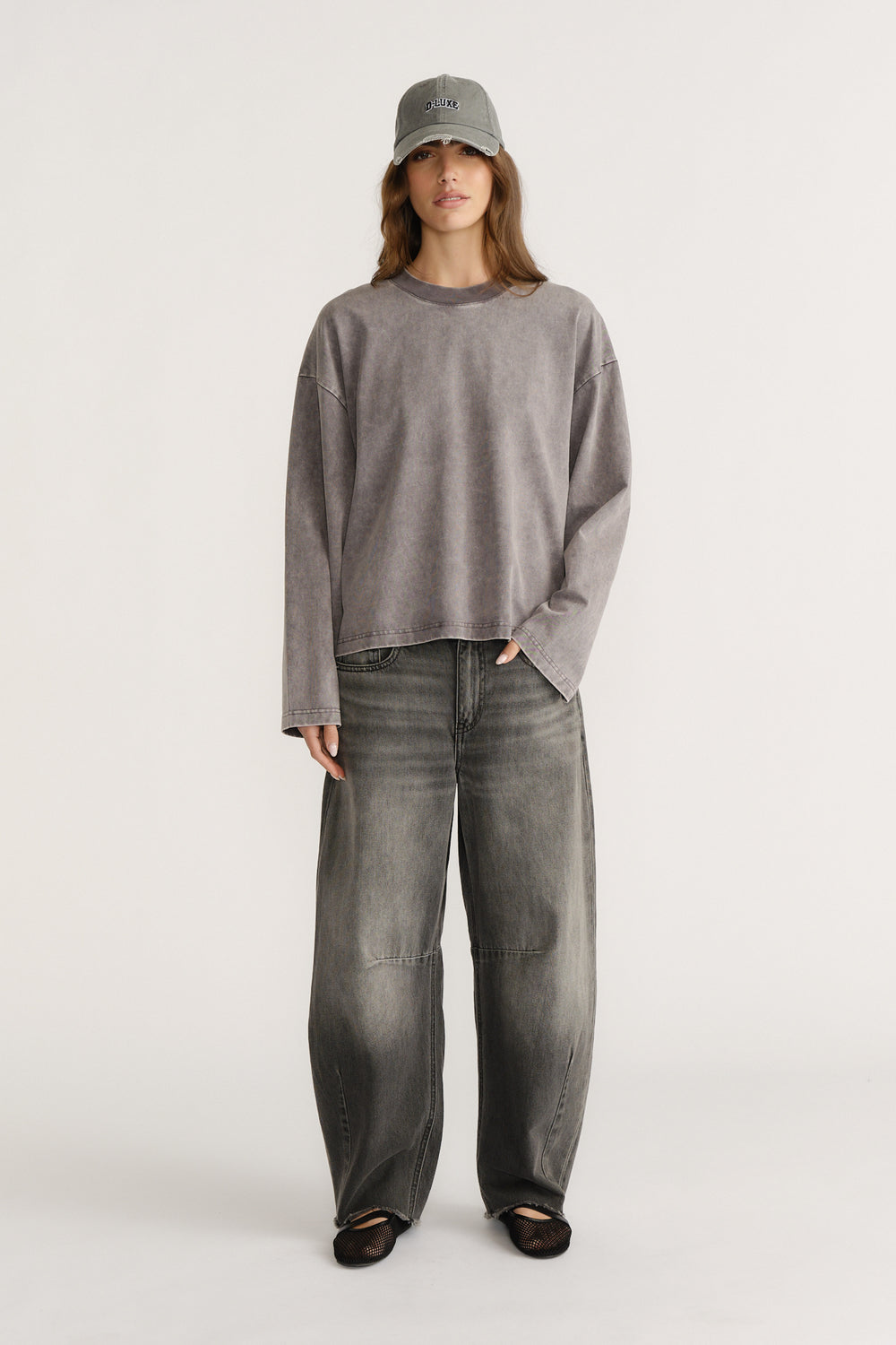 Woman wearing a washed grey long sleeve boxy tee paired with wide leg faded grey denim jeans and a grey cap