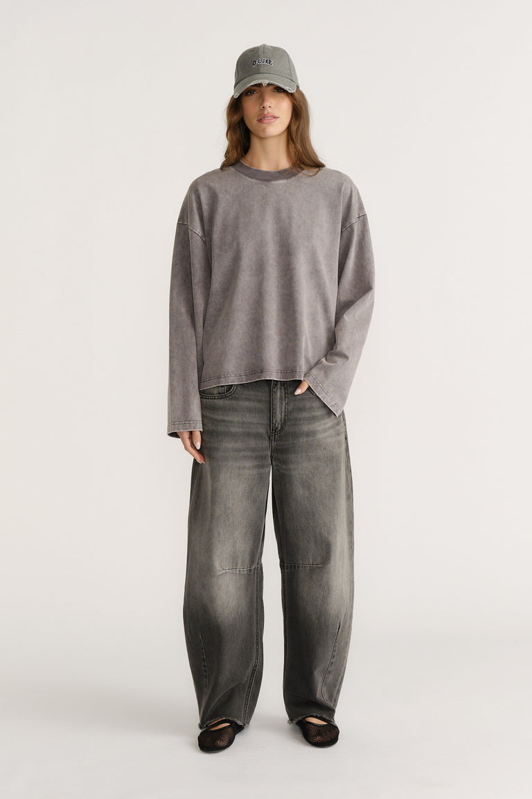 Woman wearing a washed grey long sleeve boxy tee paired with wide leg faded grey denim jeans and a grey cap