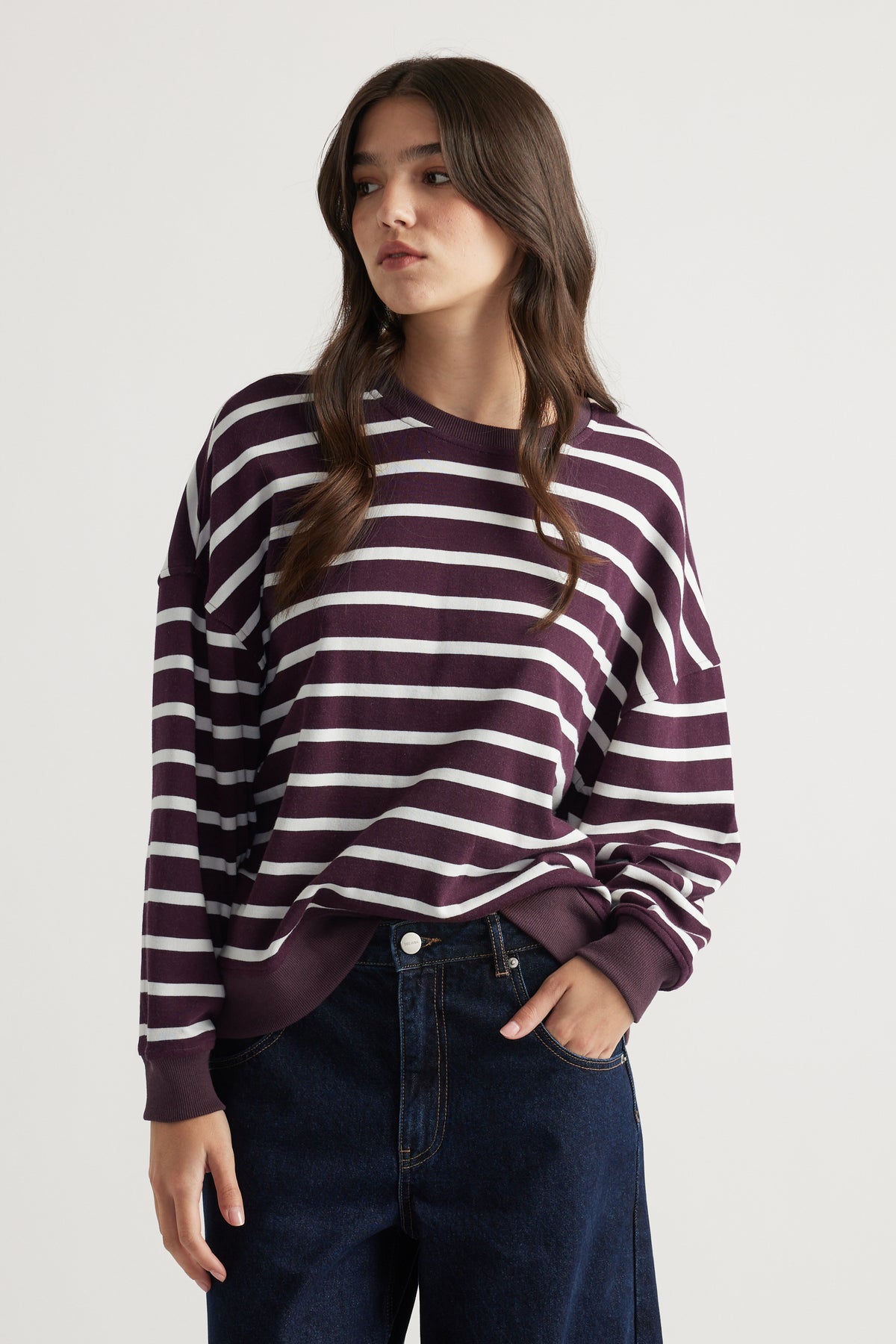 Woman wearing a relaxed-fit striped sweatshirt in deep purple paired with dark wide-leg denim jeans for a casual look