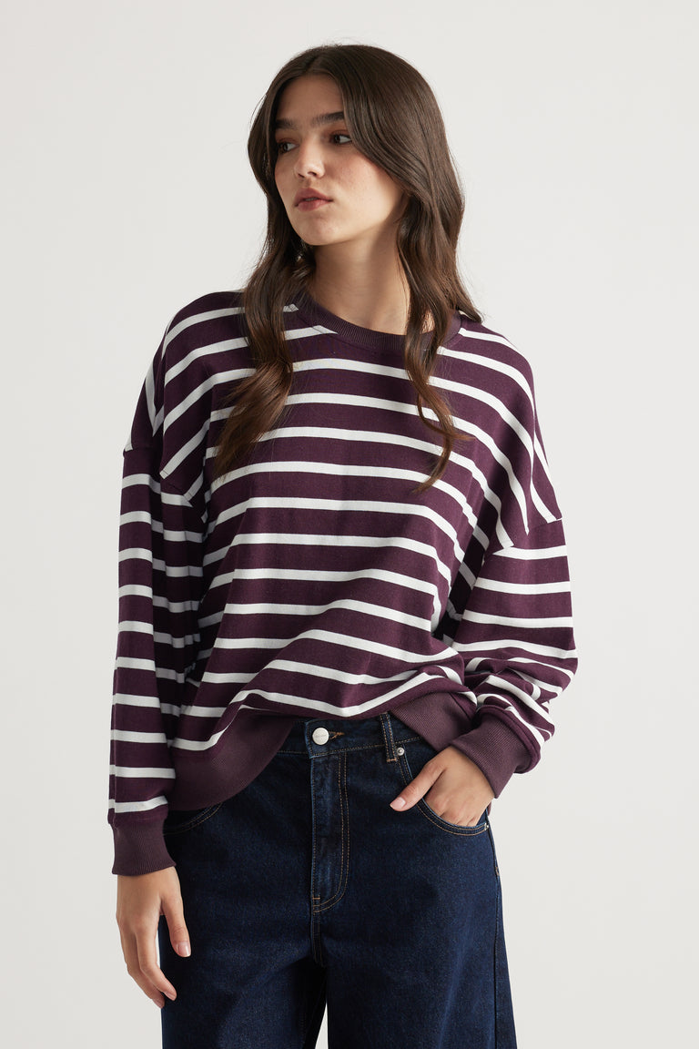 Woman wearing a relaxed-fit striped sweatshirt in deep purple paired with dark wide-leg denim jeans for a casual look