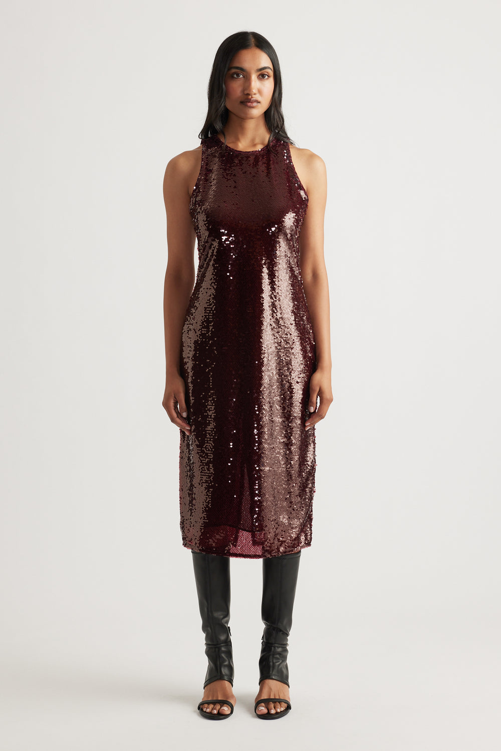 Sleeveless midi dress in deep plum covered in shimmering sequins, styled with black heeled boots for sleek elegance