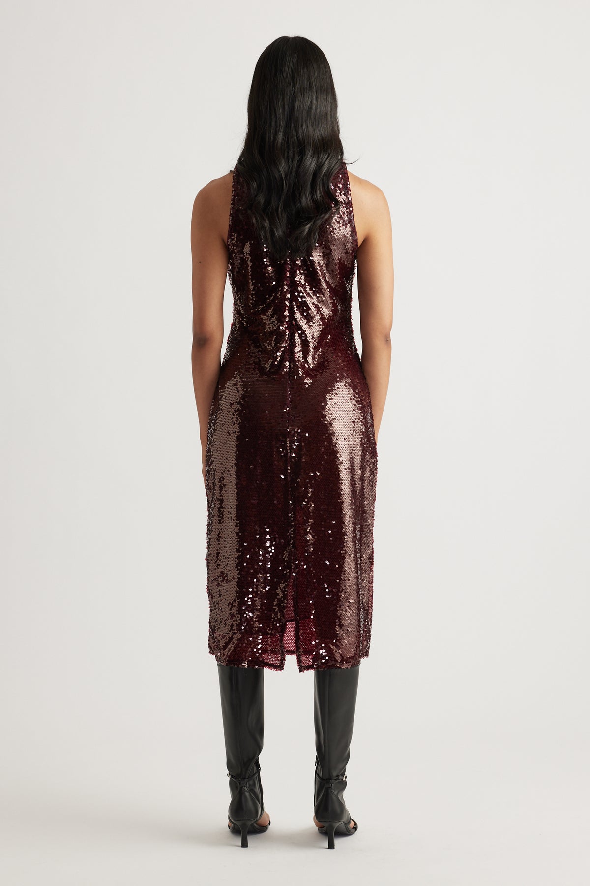 Back view of woman wearing a fitted plum sequin midi dress paired with black heeled boots