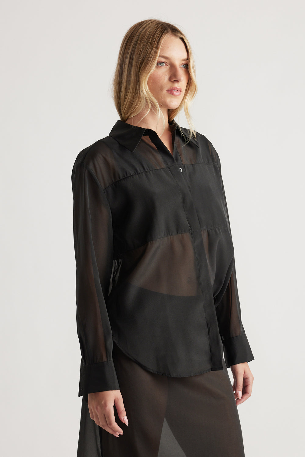 Woman wearing a black sheer organza shirt with long sleeves and a classic collar, styled in a relaxed fit