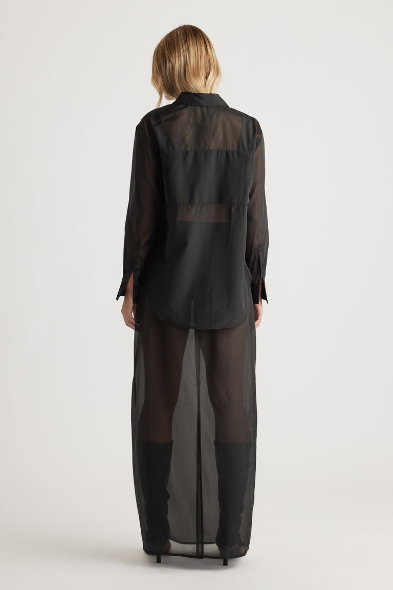 Back view of a sheer black long-sleeve shirt dress with a classic collar and layered design paired with black boots