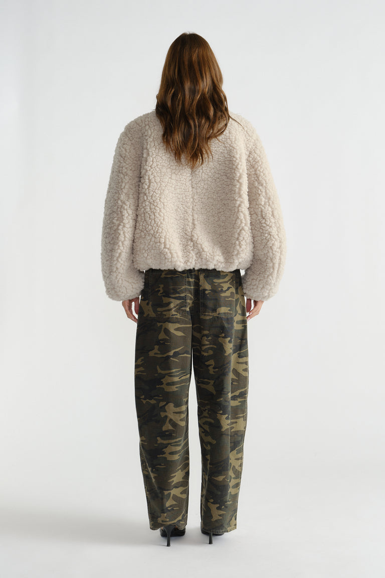 Rear view of woman wearing a soft cream sherpa bomber jacket paired with relaxed-fit camouflage pants and black heels