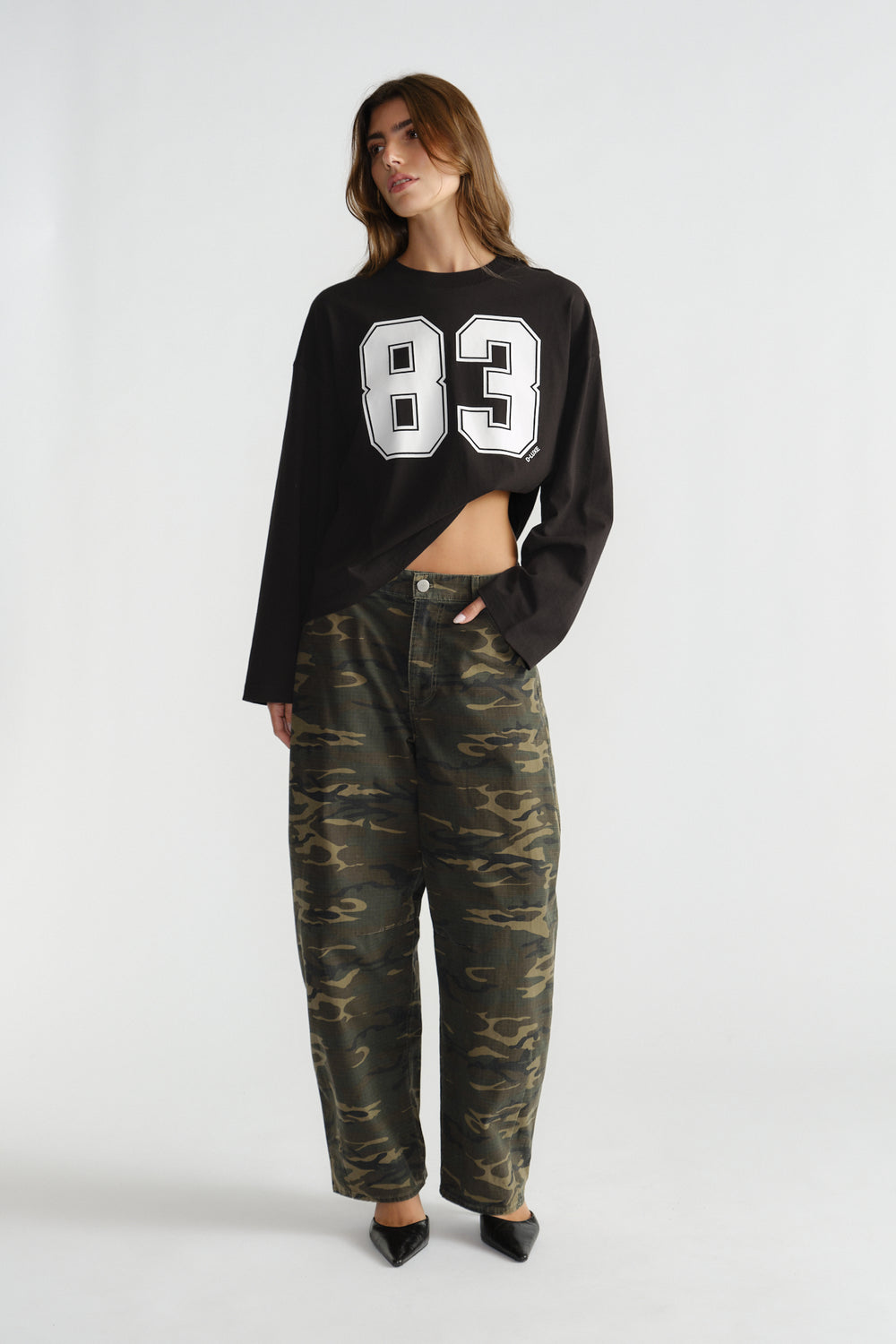 Woman wearing a black long-sleeve top with bold number print paired with relaxed camo-patterned pants and black pointed shoes