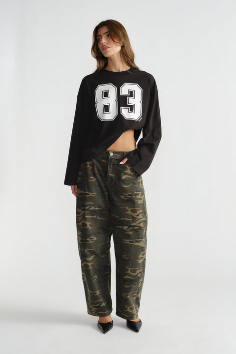 Woman wearing a black long-sleeve top with bold number print paired with relaxed camo-patterned pants and black pointed shoes
