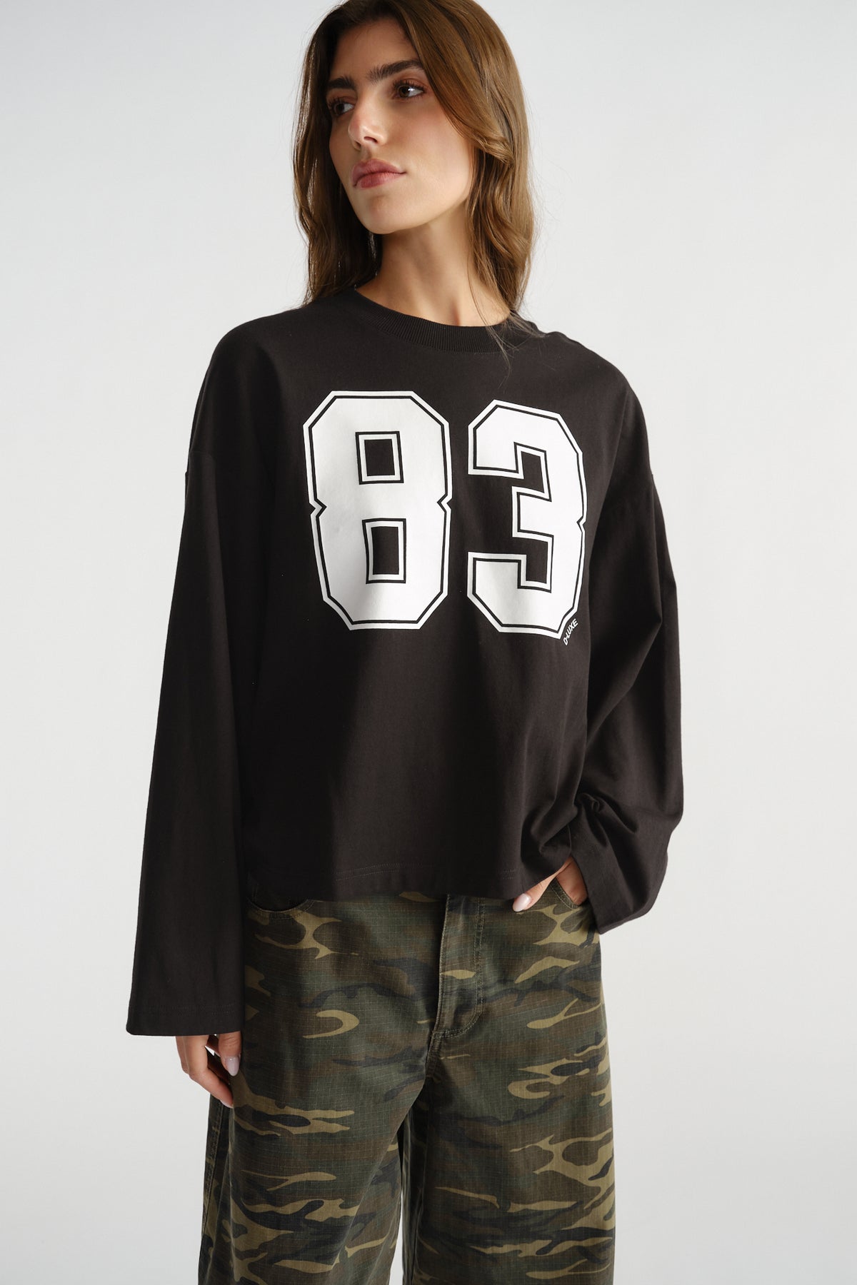 Woman wearing a black long sleeve tee with bold white number print, paired with relaxed camo pants in a casual style.