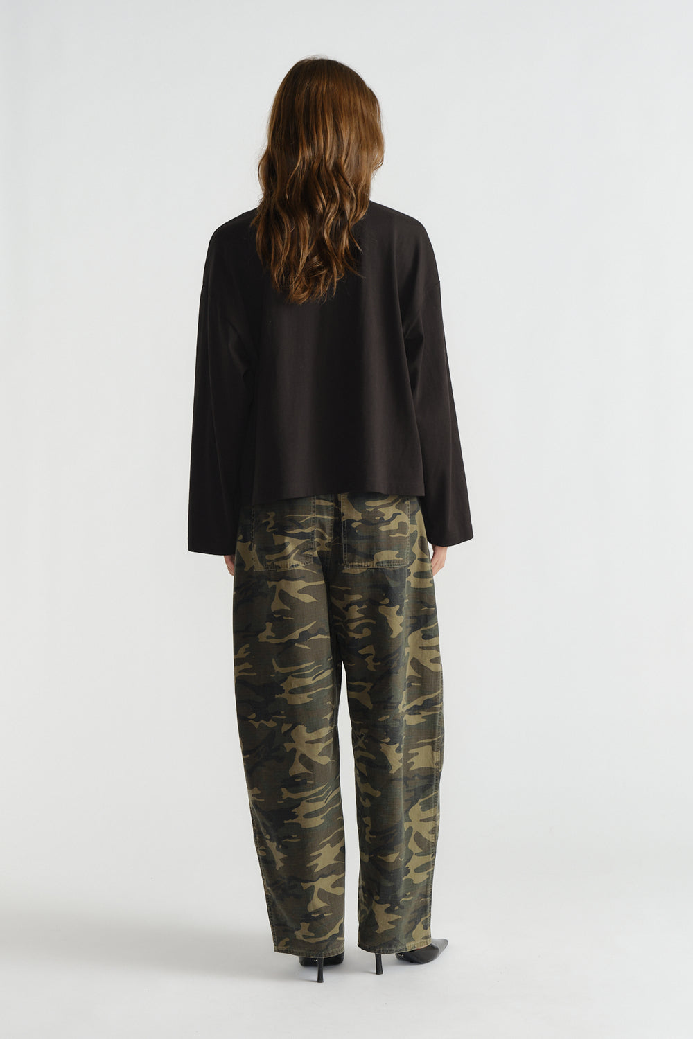 Woman seen from behind wearing a loose black long sleeve top paired with relaxed camo print pants and black heels.