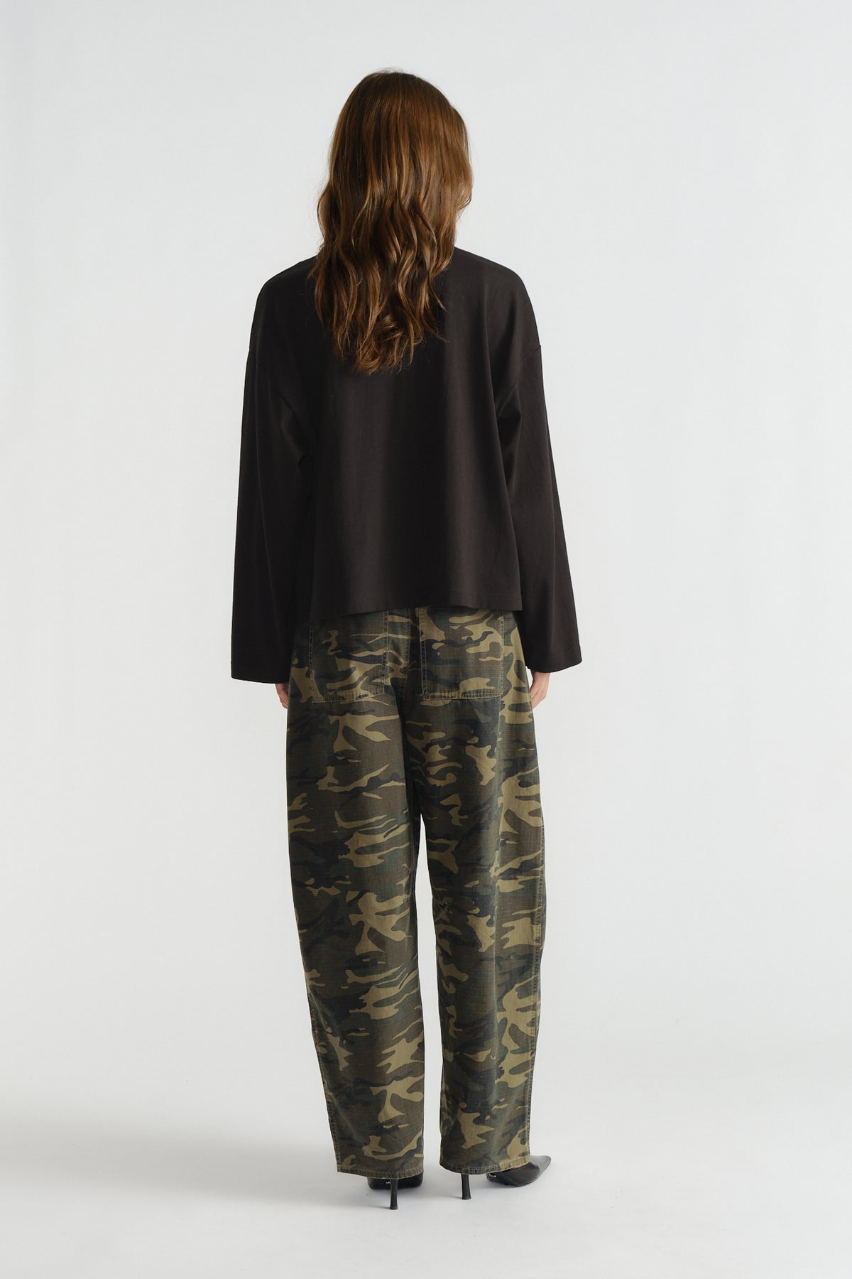 Woman seen from behind wearing a loose black long sleeve top paired with relaxed camo print pants and black heels.