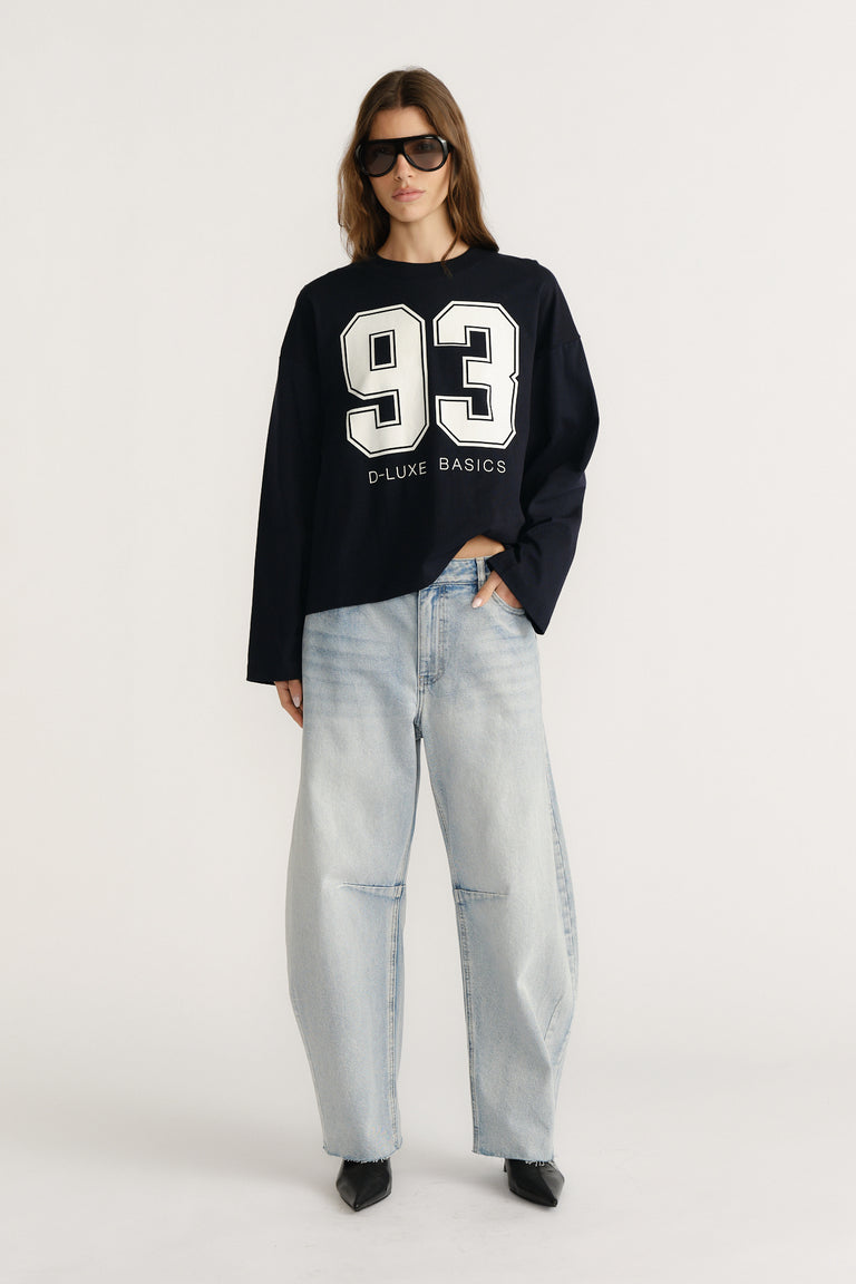 Woman wearing a navy long sleeve tee with bold white numbers paired with light wash wide-leg denim jeans and black heels