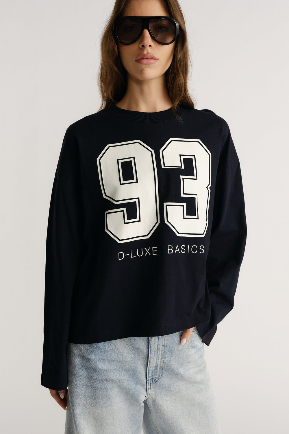 Woman wearing a navy long sleeve tee with bold white number graphic paired with light wash jeans for a casual look