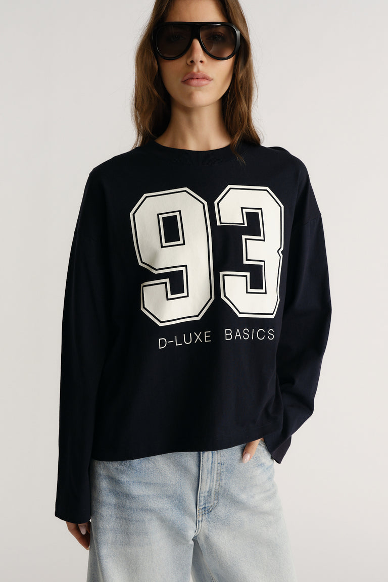 Woman wearing a navy long sleeve tee with bold white number graphic paired with light wash jeans for a casual look
