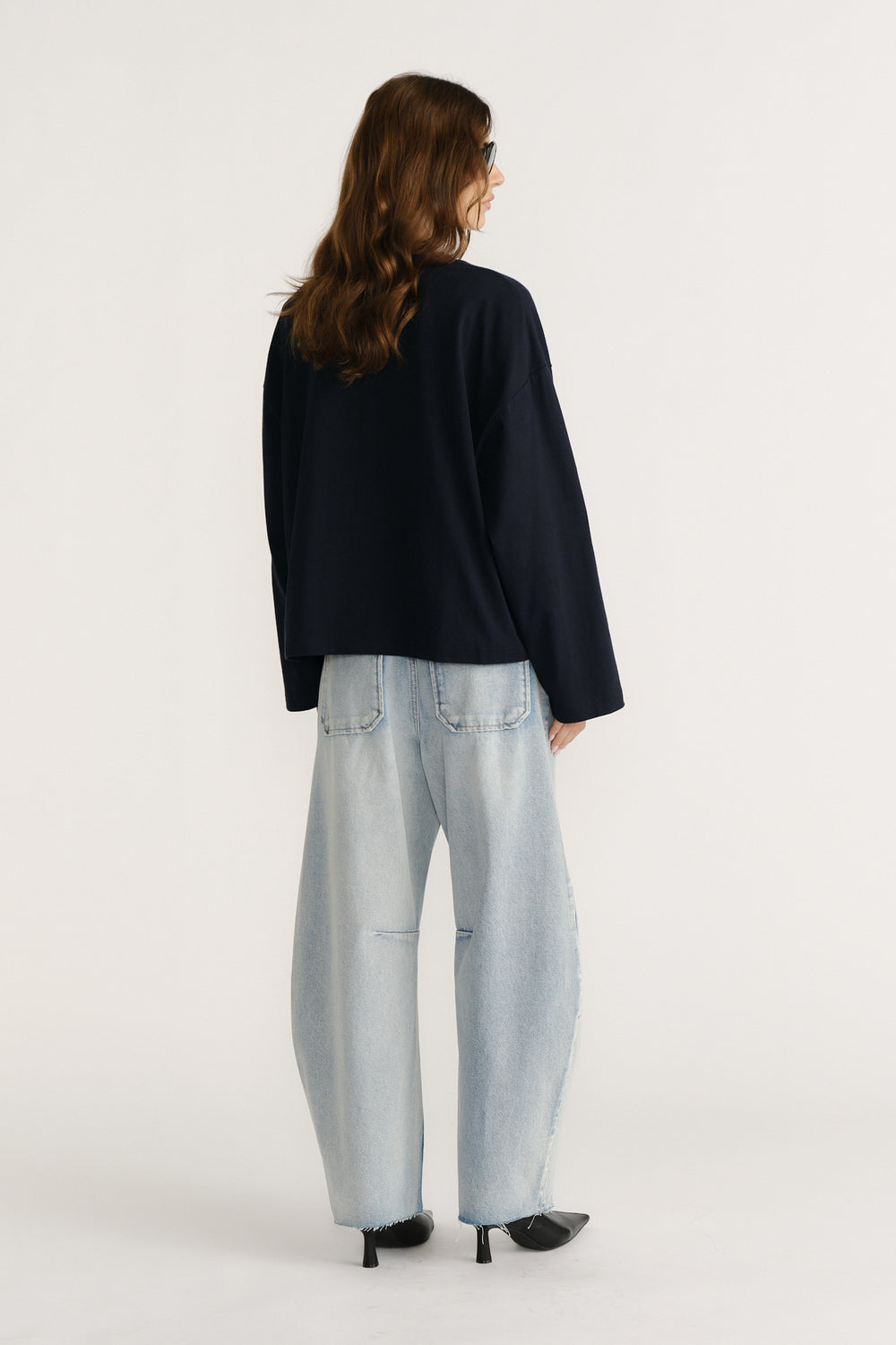 Woman wearing a relaxed navy long sleeve tee paired with light wash wide-leg jeans and black heeled shoes, back view
