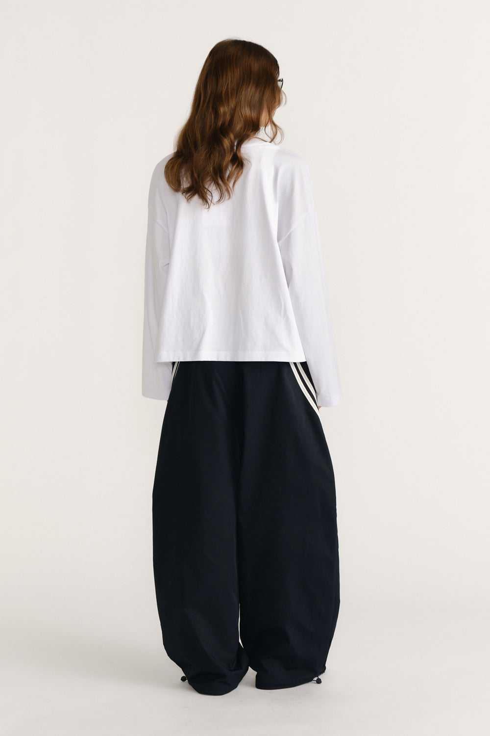 Woman shown from behind wearing a loose white long sleeve tee paired with wide-leg black pants featuring side stripe details