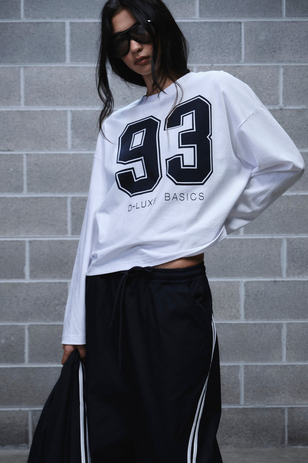 Woman wearing a white long sleeve 93 graphic tee with black track pants and side stripes