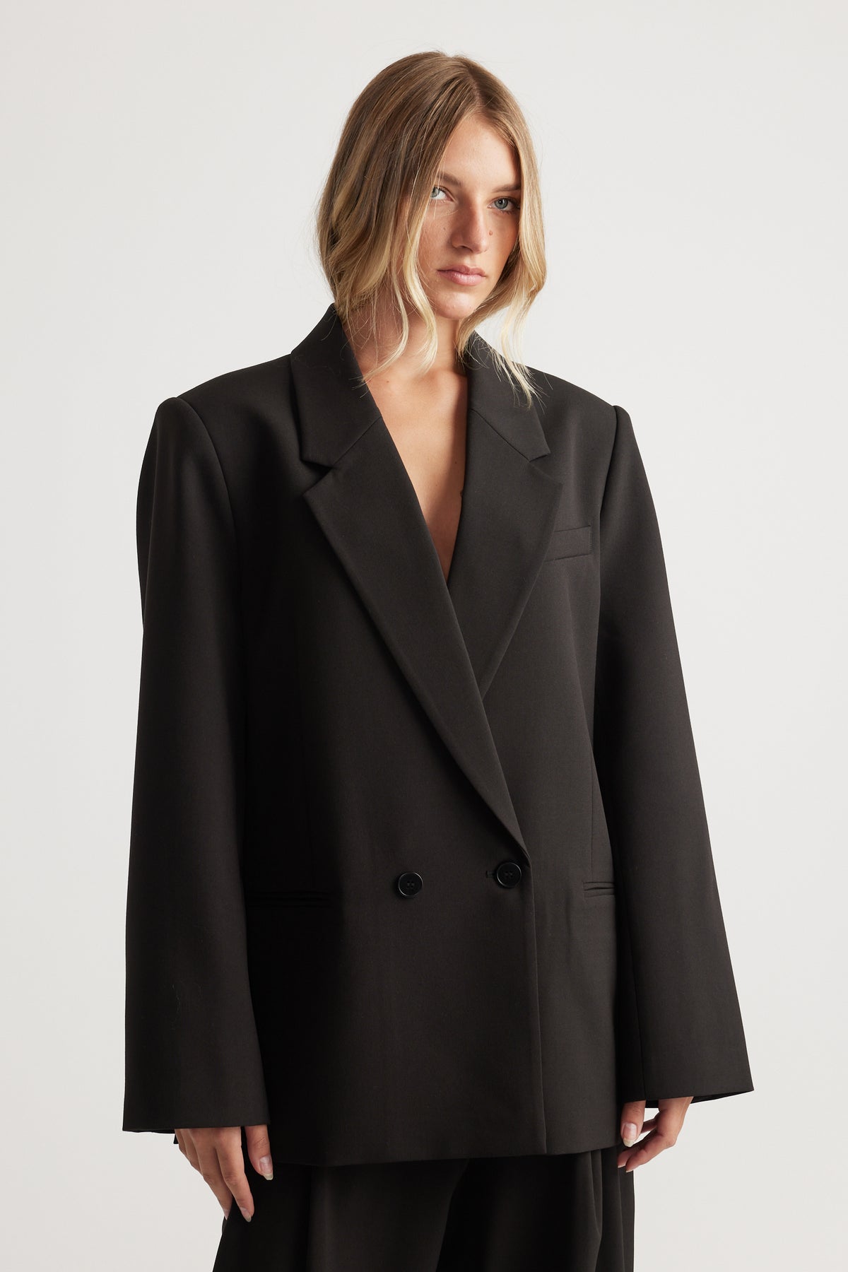 Woman wearing an oversized black double-breasted blazer with wide lapels standing against a plain background