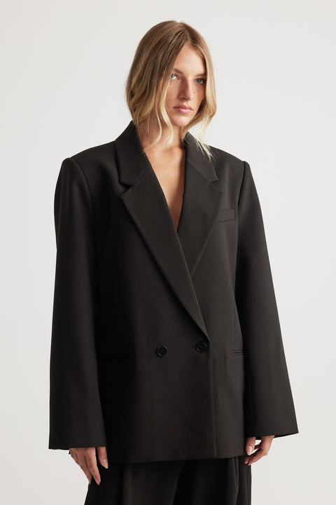 Woman wearing an oversized black double-breasted blazer with wide lapels standing against a plain background