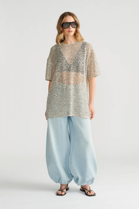 Woman wearing oversized silver sequin top paired with loose light blue denim pants and black sandals.