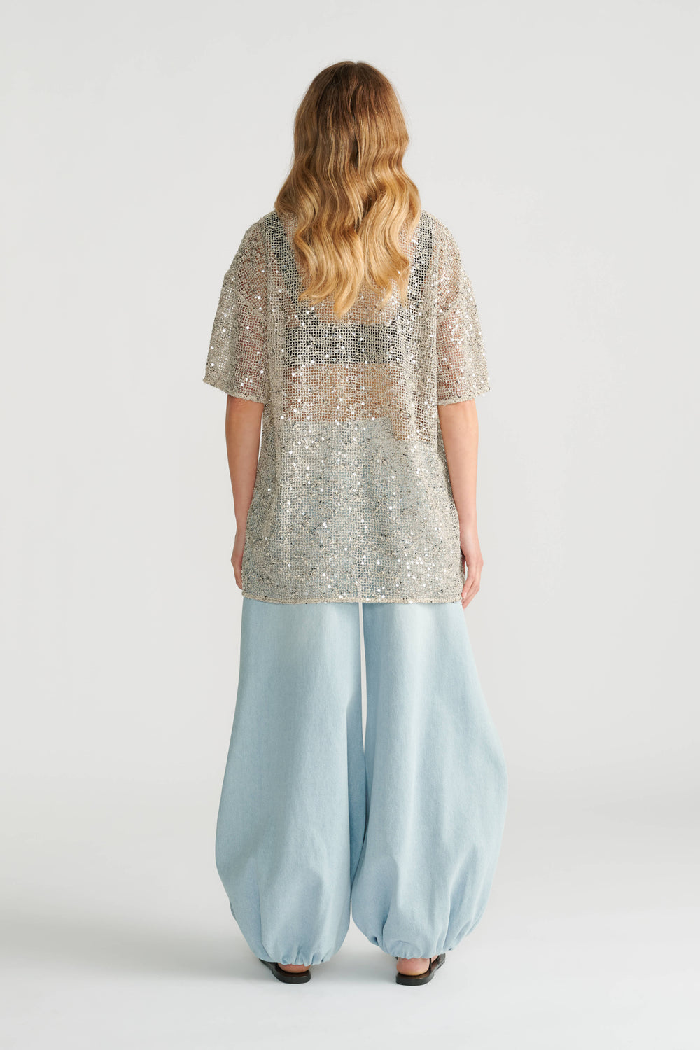 Back view of woman wearing a sparkling silver sequin top paired with loose, light blue wide-leg pants