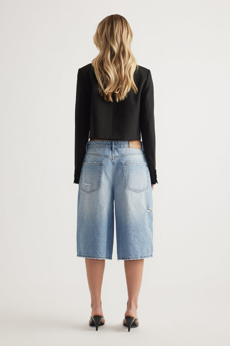 Back view of a model wearing light blue denim shorts with a straight knee length fit and back pockets
