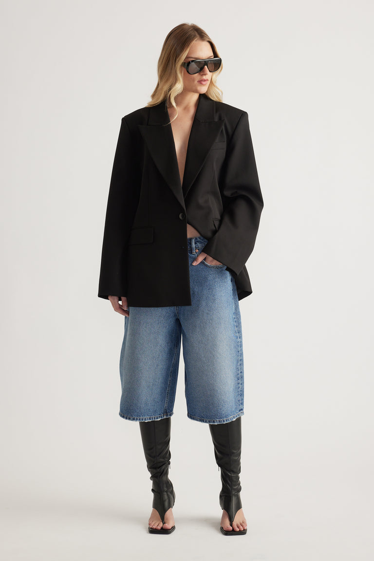 Woman wearing a black blazer with longline denim shorts, sunglasses and black heeled boots
